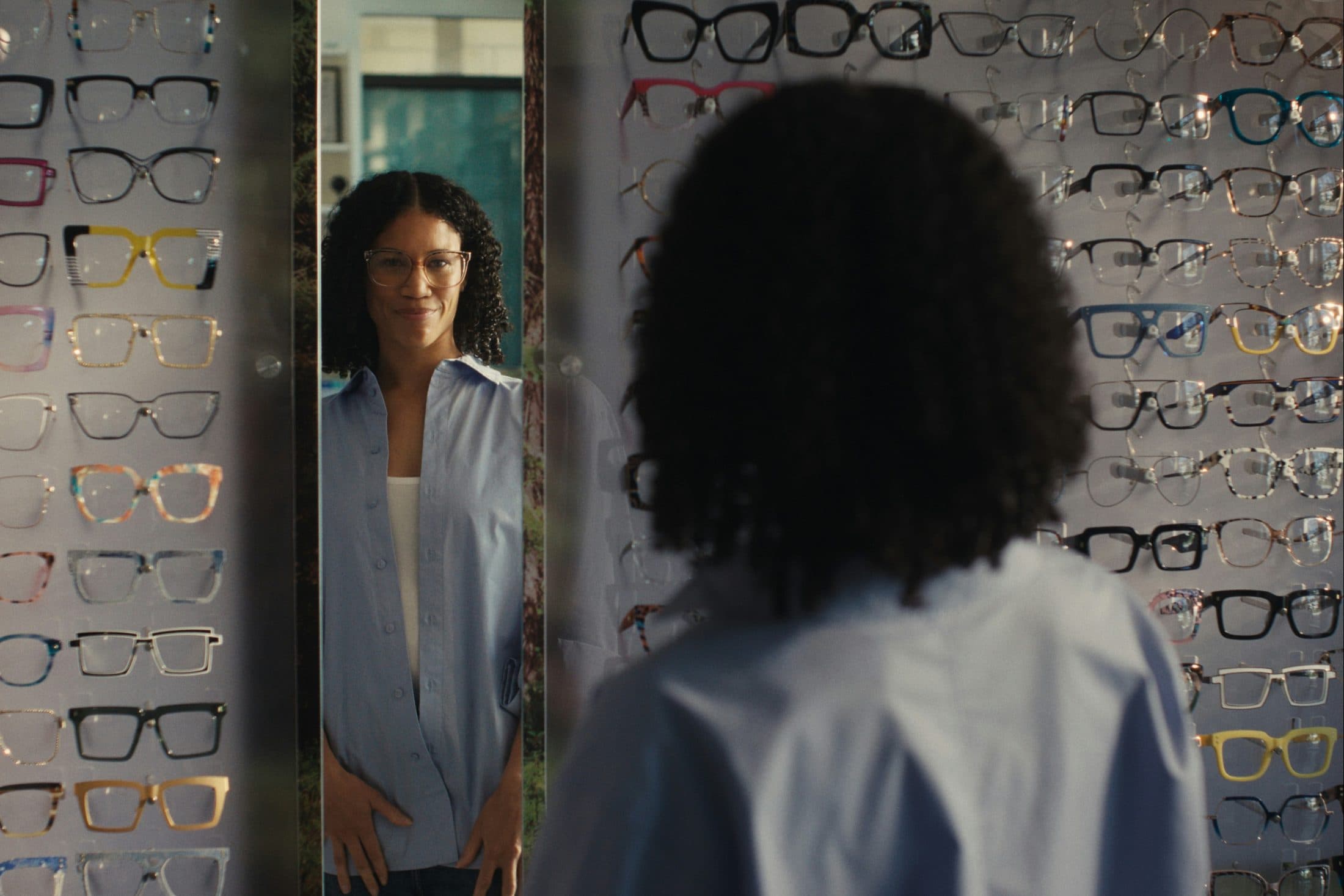 Une cliente devant un miroir, entourée de murs de montures