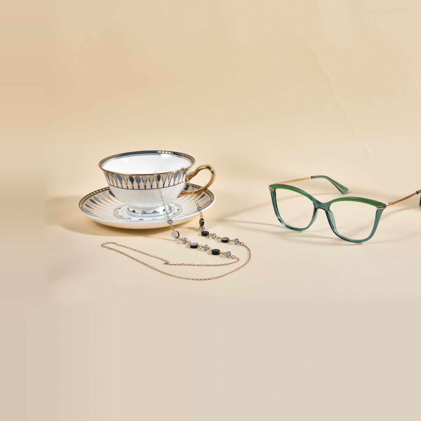 Chaînette dorée à perles posée sur une tasse en porcelaine, à côté d'une monture verte transparente
